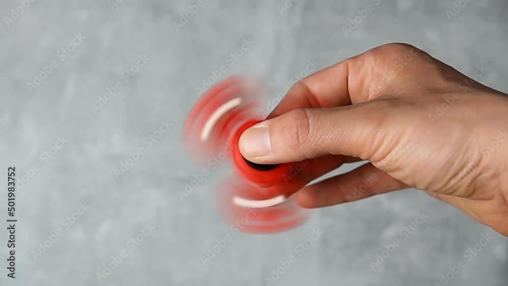 Man hand rotating red plastic fidget spinner on marble background. Anti stress toy