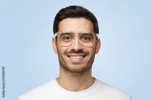 Attractive smiling handsome man in t-shirt and eyeglasses isolated on blue background © Damir Khabirov