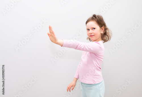 Child, Caucasian 6 years old, in a pink coat on a gray background. The child is stressed, shows a stop gesture with his hands, he is not happy.