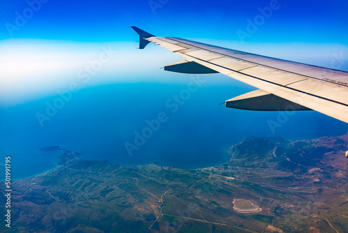 View from the airplane window at a beautiful blue clear sky, earth, sea and the airplane wing