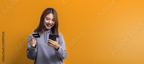 Canvastavla Portrait of beautiful Asian woman holding credit card and mobile phone on isolated yellow background, portrait concept used for advertisement and signage, isolated over background, copy space