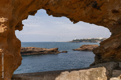 View of Biarritz coastline and lighthouse through window washed in stone by sea for millennia. Pyrenees-Atlantiques department, French Basque Country © Artem