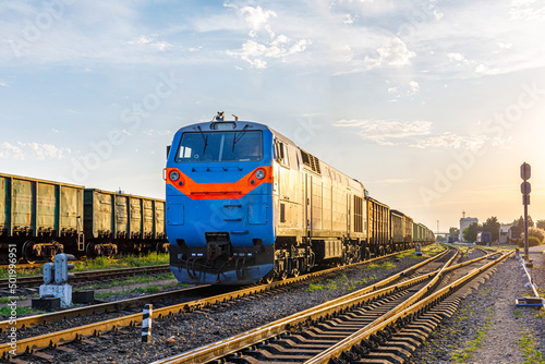 A powerful locomotive with a freight train departs from the marshalling railway station. Sunset lighting.