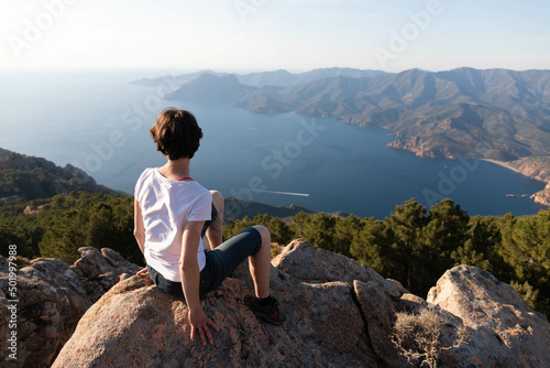 Young woman sitting alone in front of a breathtaking panoramic landscape at sunset in Corsica  meditation position