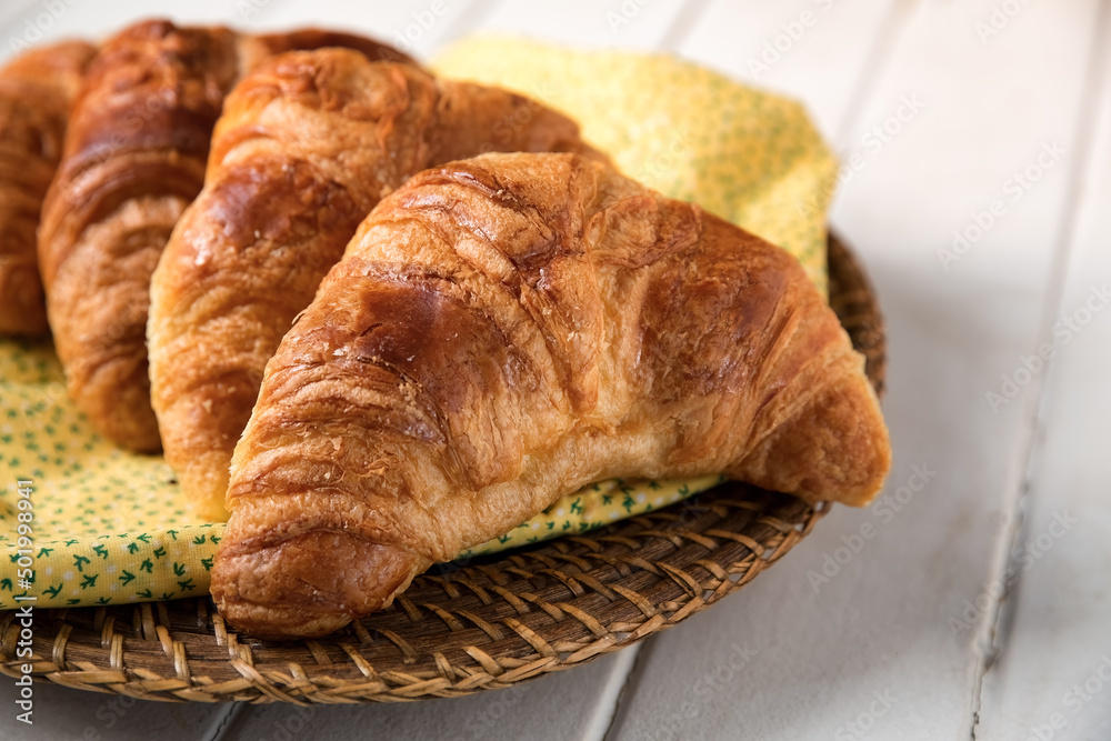 Fresh croissant, on a yellow and green napkin and wicker basket. Low angle view with space for text. Fresh croissant, on a yellow and green napkin and wicker basket. Low angle view with space for text.