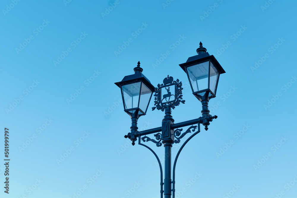 Street lamps in retro style with coat of arms of Nizhny Novgorod against blue sky.