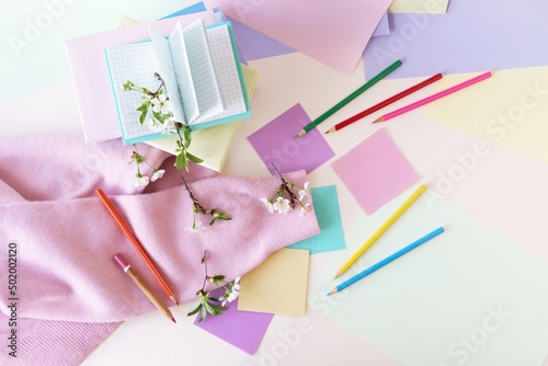 A stack of books, textbooks, pencils, notepads and twigs of cherry blossoms on a table, against a background of colored paper in pastel colors, the concept of learning, education, back to school 