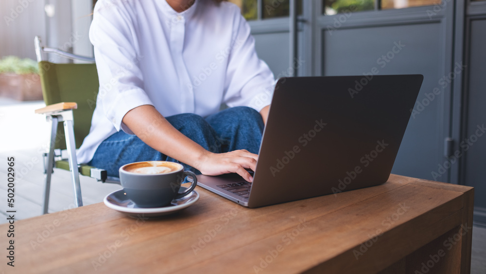 Closeup image of a woman using and working on laptop computer with coffee cup on the table Closeup image of a woman using and working on laptop computer with coffee cup on the table