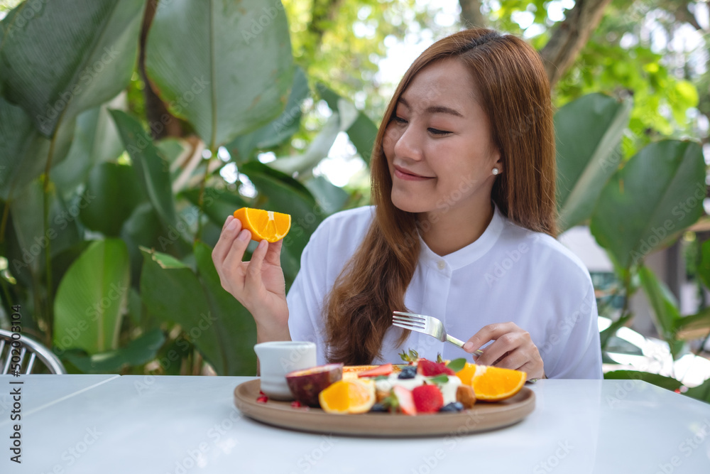 Portrait image of a young woman holding a piece of an orange while eating mixed fruits french toast brunch in restaurant Portrait image of a young woman holding a piece of an orange while eating mixed fruits french toast brunch in restaurant