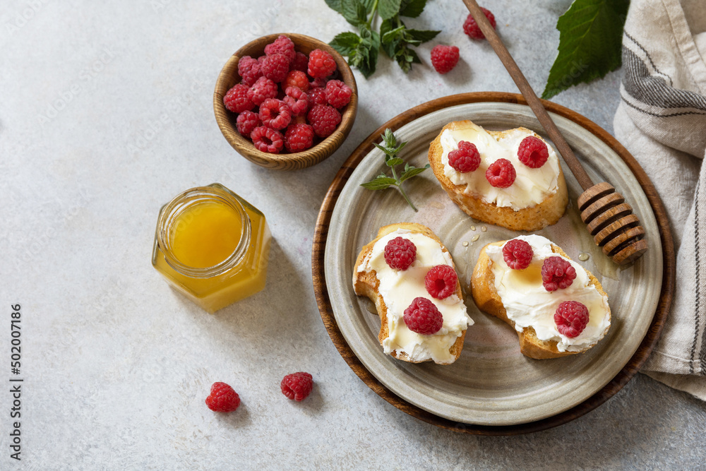 Healthy summer breakfast with sweet sandwiches with ricotta, raspberries and honey on a stone table. Copy space. Healthy summer breakfast with sweet sandwiches with ricotta, raspberries and honey on a stone table. Copy space.