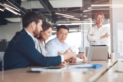 Smiling confident businesswoman wearing eyeglasses on business meeting with colleagues in office 