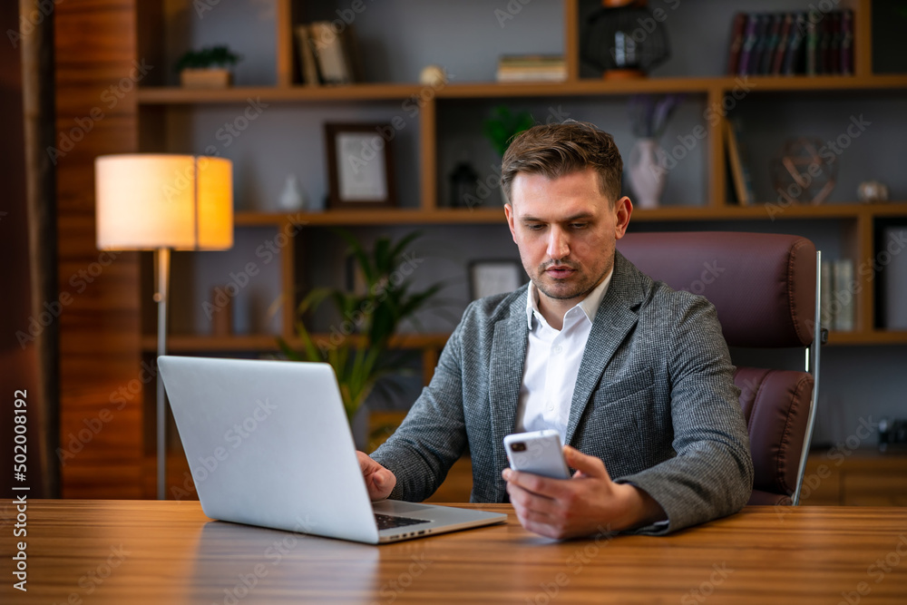Young business man working at office with laptop and uses a smartphone Young business man working at office with laptop and uses a smartphone