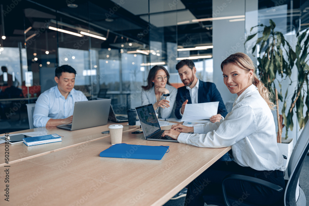 confident smiling businesswoman sitting at the office with group of colleagues, on background. 