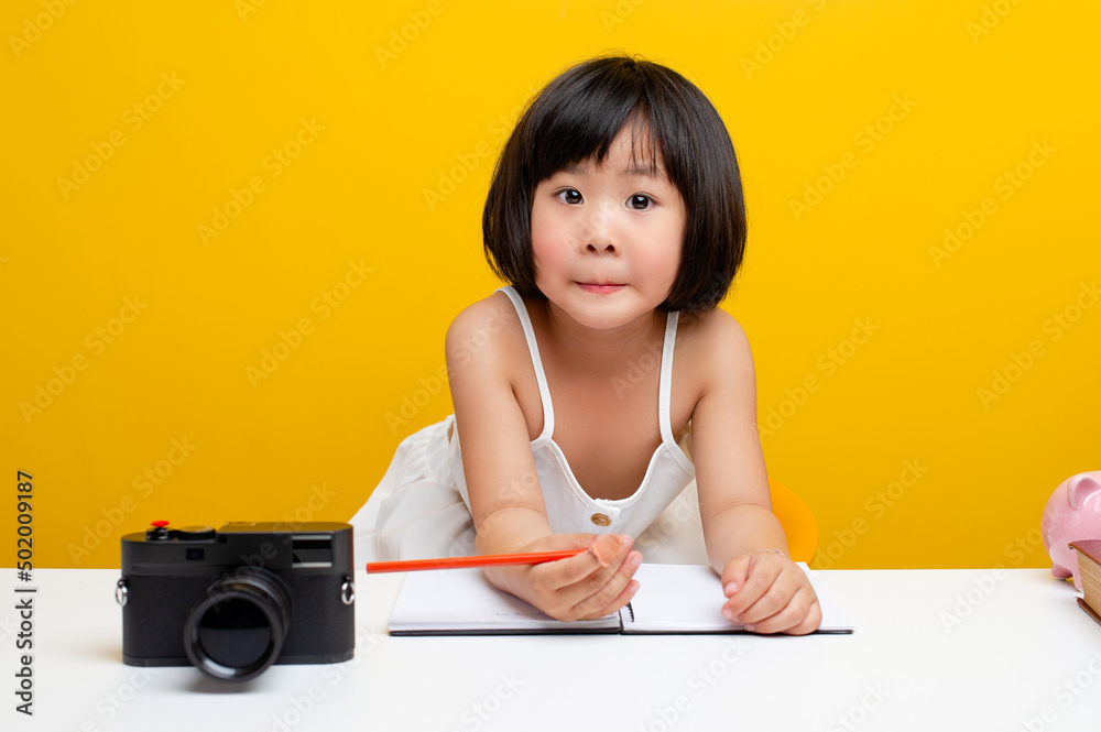 cute girl pictures Asia writes a book In the office for hardworking kids. Smart kids. White table on a yellow background. cute girl pictures Asia writes a book In the office for hardworking kids. Smart kids. White table on a yellow background.