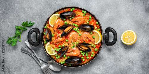 Traditional Spanish paella with seafood in a frying pan. Gray concrete grunge background. Top view, flat lay. Mediterranean food. Banner