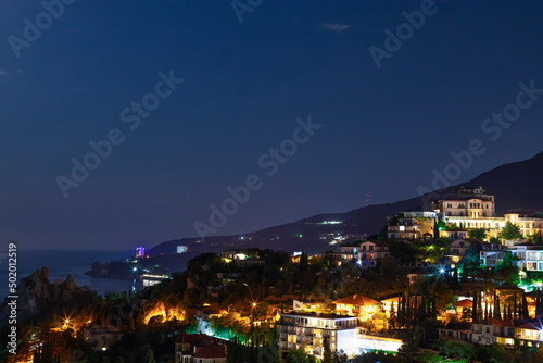 Night city view on coast of mediterranean sea with lights illumination on colorful houses.