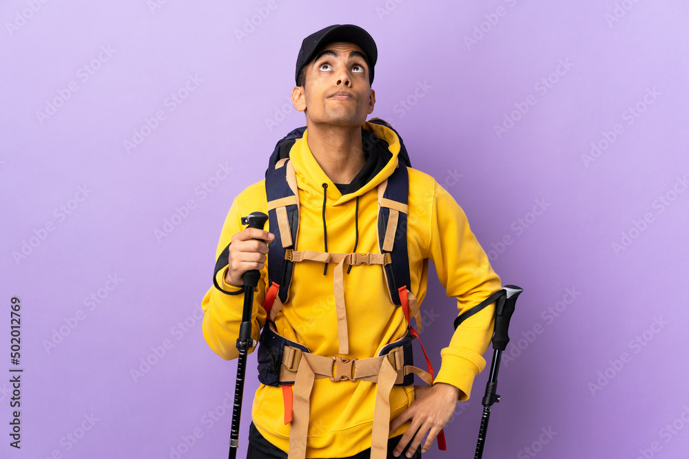 African American man with backpack and trekking poles over isolated background and looking up African American man with backpack and trekking poles over isolated background and looking up