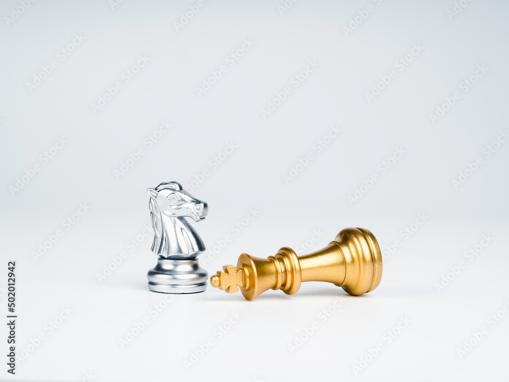 The silver horses, knight chess piece standing near the loser golden king chess piece who fell isolated on white background. Leadership, winner, loser, competition, and business strategy concept. The silver horses, knight chess piece standing near the loser golden king chess piece who fell isolated on white background. Leadership, winner, loser, competition, and business strategy concept.