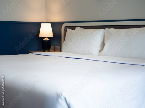 Four white clean pillows, blanket and linen bed sheet in the hotel room with copy space. Bedding near the lamp in the bedroom.