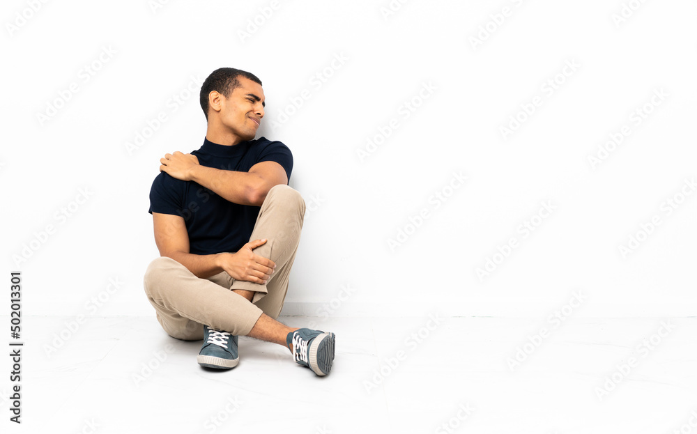 African American man sitting on the floor suffering from pain in shoulder for having made an effort