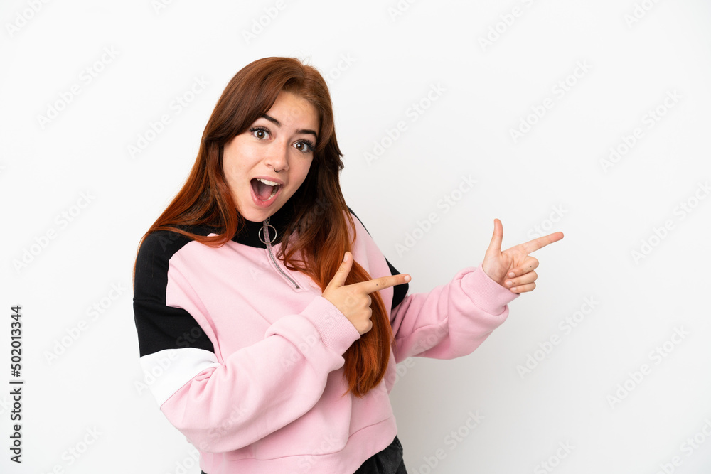 Young redhead woman isolated on white background surprised and pointing side Young redhead woman isolated on white background surprised and pointing side