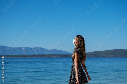 Young woman with a medical protective mask on her face standing by the sea