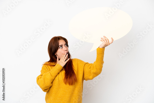 Young redhead woman isolated on white background holding an empty speech bubble with surprised expression