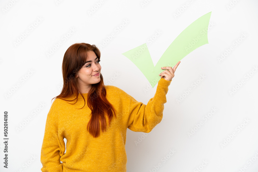Young redhead woman isolated on white background holding a check icon with happy expression Young redhead woman isolated on white background holding a check icon with happy expression