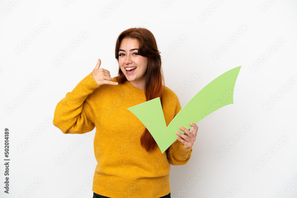 Young redhead woman isolated on white background holding a check icon and doing phone gesture Young redhead woman isolated on white background holding a check icon and doing phone gesture