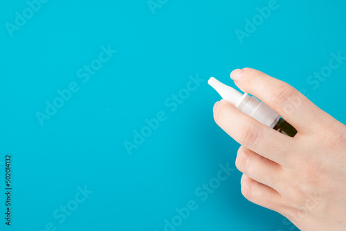 nasal drops, cold treatment, spray for nose in hand on a blue background with copy space