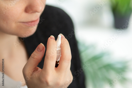 drops in the nose, a woman holds a bottle with a nasal spray for a cold