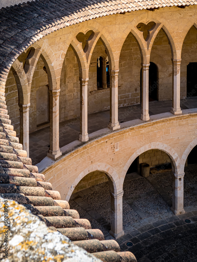 Portrait photography of the patio of castle Castell de Bellver in Palma de Mallorca with romanesque style arcade in the lower floor and gothic style colonnade in the upper floor built with limestone.