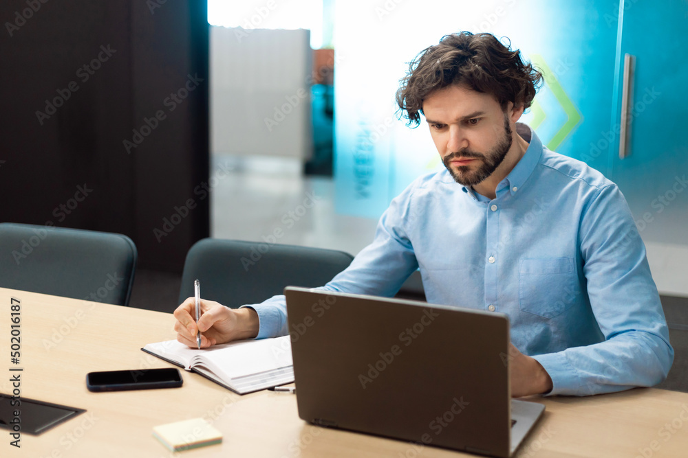 Portrait of focused man using laptop and writing in notebook Portrait of focused man using laptop and writing in notebook