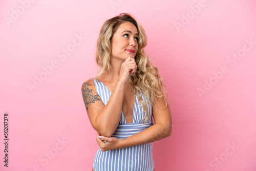 Young Brazilian woman in swimsuit in summer holidays isolated on pink background and looking up