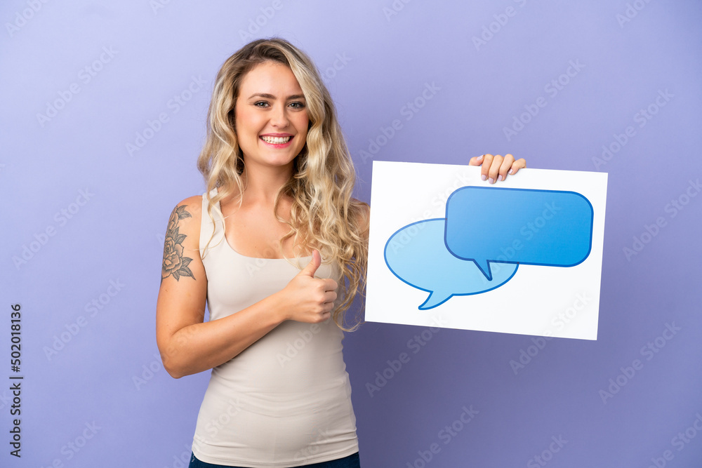 Young Brazilian woman isolated on purple background holding a placard with speech bubble icon with thumb up Young Brazilian woman isolated on purple background holding a placard with speech bubble icon with thumb up