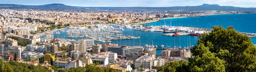 Wide panorama photography of the bay of Palma de Mallorca with docks, marina, city, old town, cathedral La Seu, airport and garden city beach Playa Ciudad Jardín at the horizon on a springtime day.