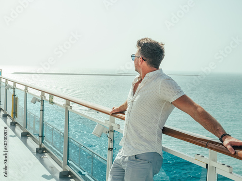 Fashionable man standing on the empty deck of a cruise liner against the backdrop of the setting sun. Closeup, outdoor. Vacation and travel concept