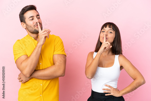 Young couple isolated on pink background showing a sign of closing mouth and silence gesture