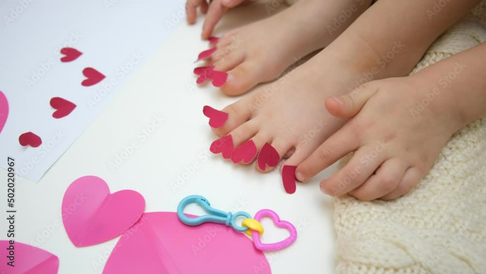 Child playing with adhesive tape paper, funny pedicure with small hearts Child playing with adhesive tape paper, funny pedicure with small hearts