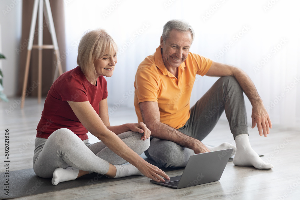 Sporty senior man and woman training at home, using notebook