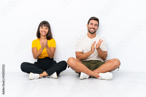 Young couple sitting on the floor isolated on white background applauding after presentation in a conference