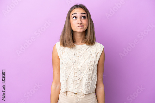 Young caucasian woman isolated on purple background and looking up