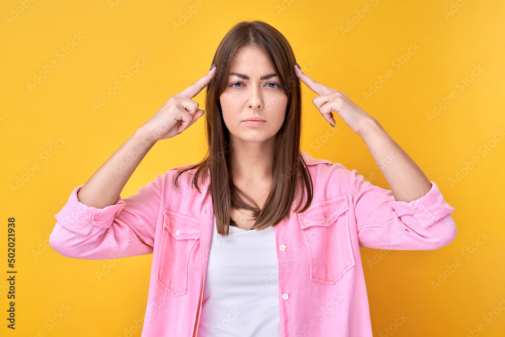 Smart brunette girl in casual holding her head thinks doubts, makes decision isolated on yellow studio background