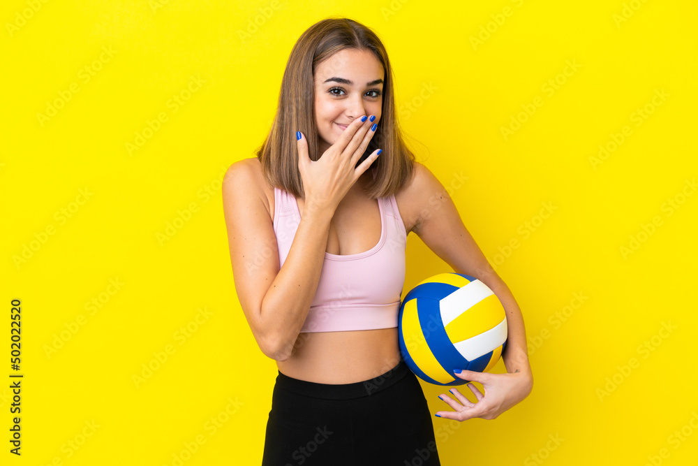 Young woman playing volleyball isolated on yellow background happy and smiling covering mouth with hand Young woman playing volleyball isolated on yellow background happy and smiling covering mouth with hand
