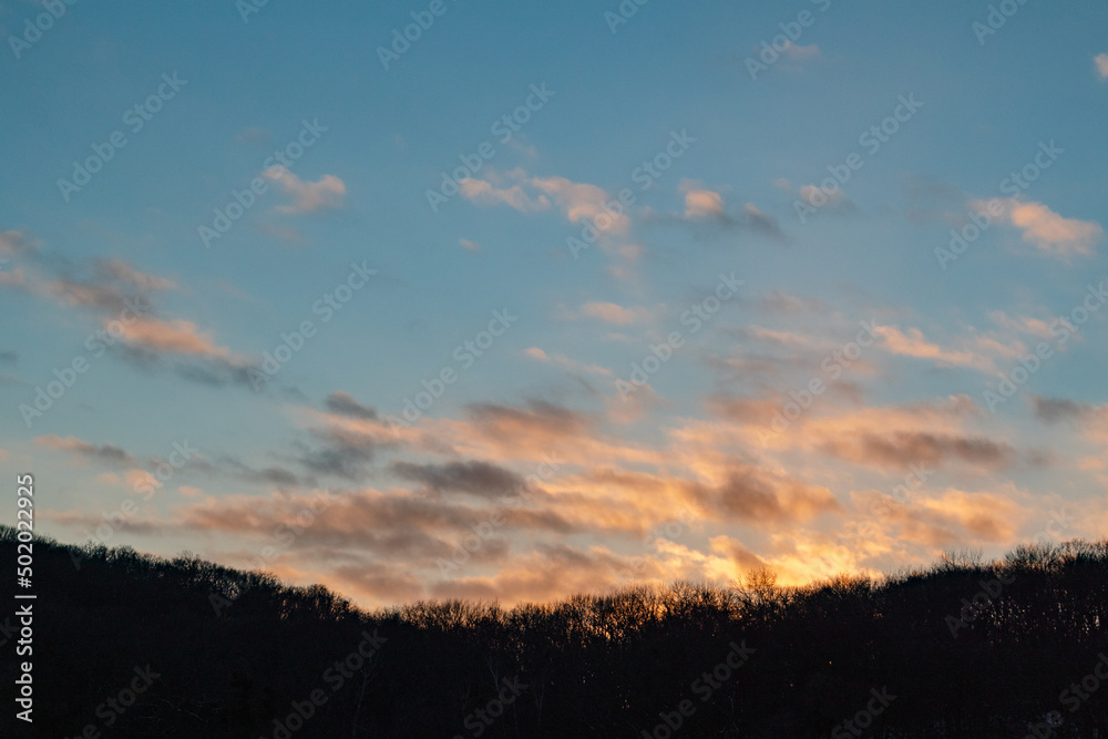 Dramatic sunset sky clouds above trees silhouette background. Evening vivid colored cloudy blue countryside view