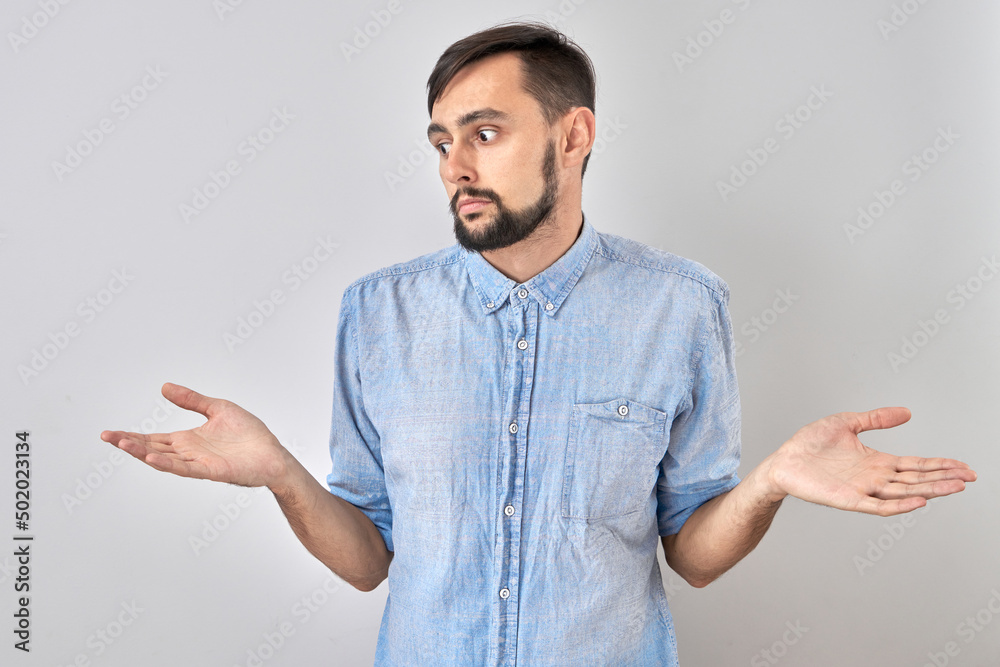 Smart brunette man in casual shrugging hands thinks doubts, makes decision isolated on blue studio background Smart brunette man in casual shrugging hands thinks doubts, makes decision isolated on blue studio background