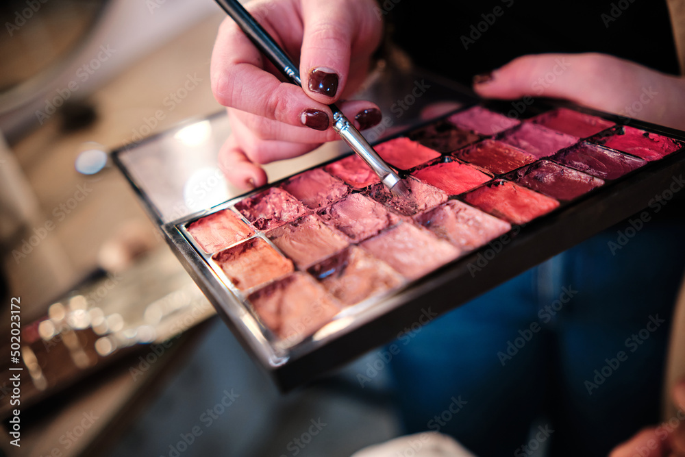 Close up view of a professional makeup artist using a lipstick palette while applying makeup. - obrazy, fototapety, plakaty 