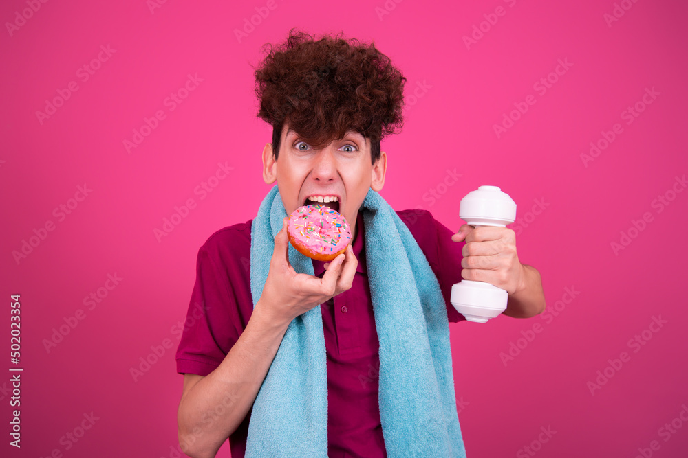 Sport and retro style. Young attractive guy on a pink background with dumbbells and a donut. Sport and retro style. Young attractive guy on a pink background with dumbbells and a donut.