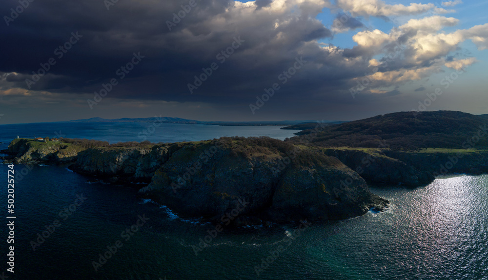 Panorama view from above on rocky ledge with stones and vegetation washed by the Black Sea in Bulgaria under cloudy sky
