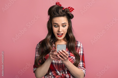 Shocked young pinup lady in retro outfit looking at smartphone screen, winning lottery or online casino bet